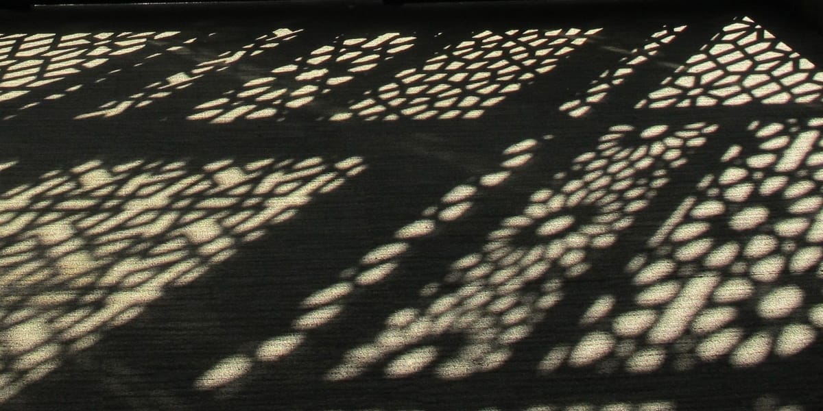 Patterns of sunlight and a shadow from a mashrabiya lattice window on the floor.